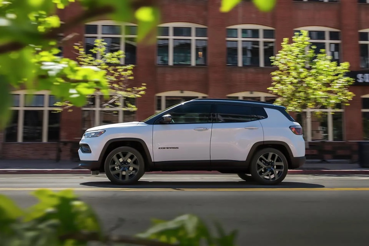Jeep Compass 2026 blanc vu de profil en environnement urbain devant un immeuble en briques, soulignant le format pratique et l’intégration au quotidien.
