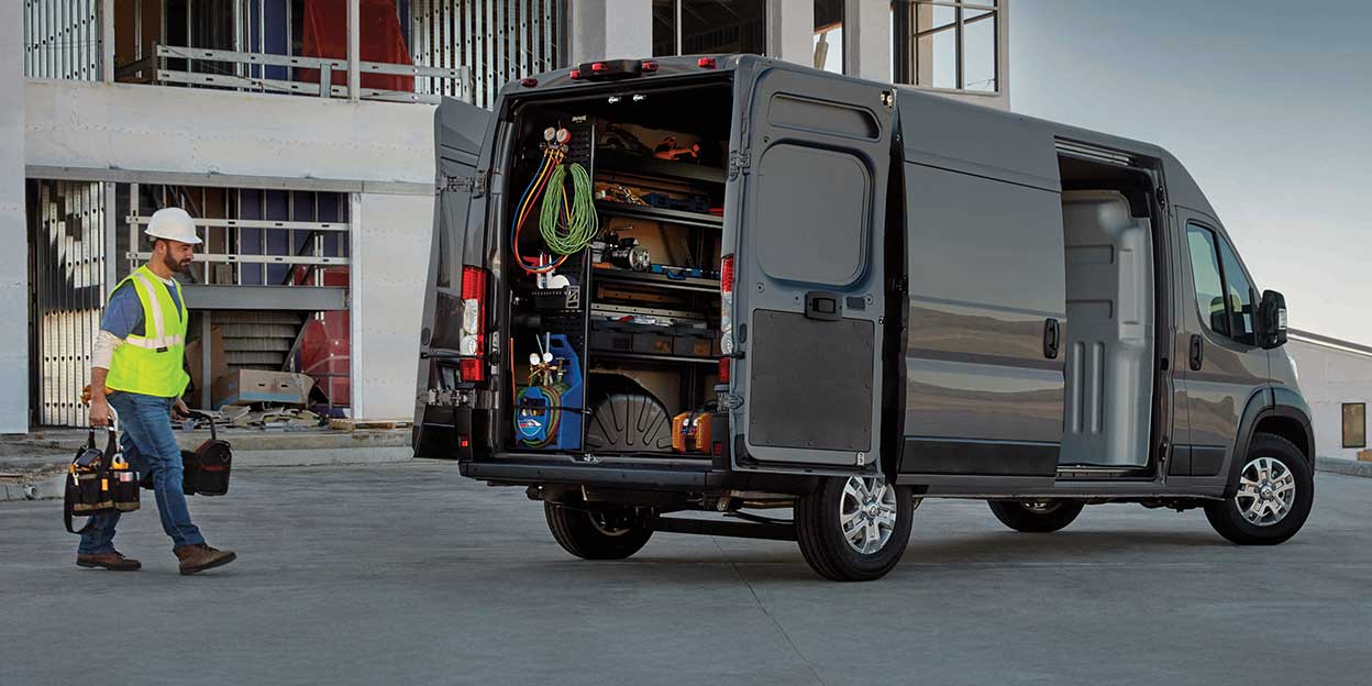 Vue arrière du Ram ProMaster 2026 avec portes ouvertes, montrant un aménagement utilitaire complet rempli d’outils sur un chantier urbain.