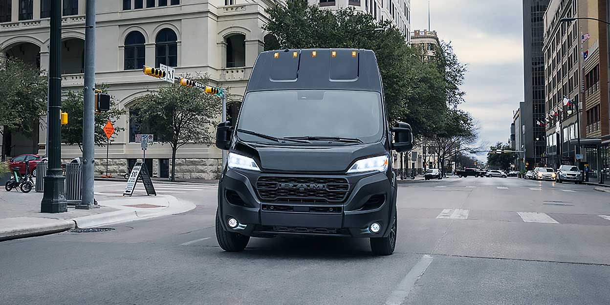 Vue de face du Ram ProMaster 2026 noir circulant en milieu urbain, avec phares allumés et design utilitaire robuste.