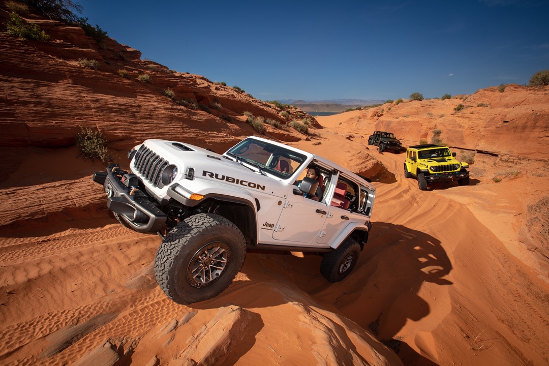 Trois Jeep Wrangler qui montent sur des rochers dans le désert.