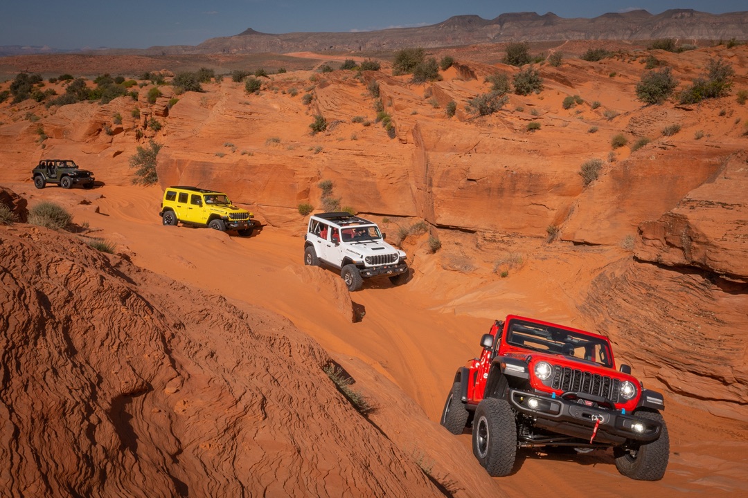 Quatre Jeep Wrangler qui roulent sur une route dans le désert pleine de rocher.