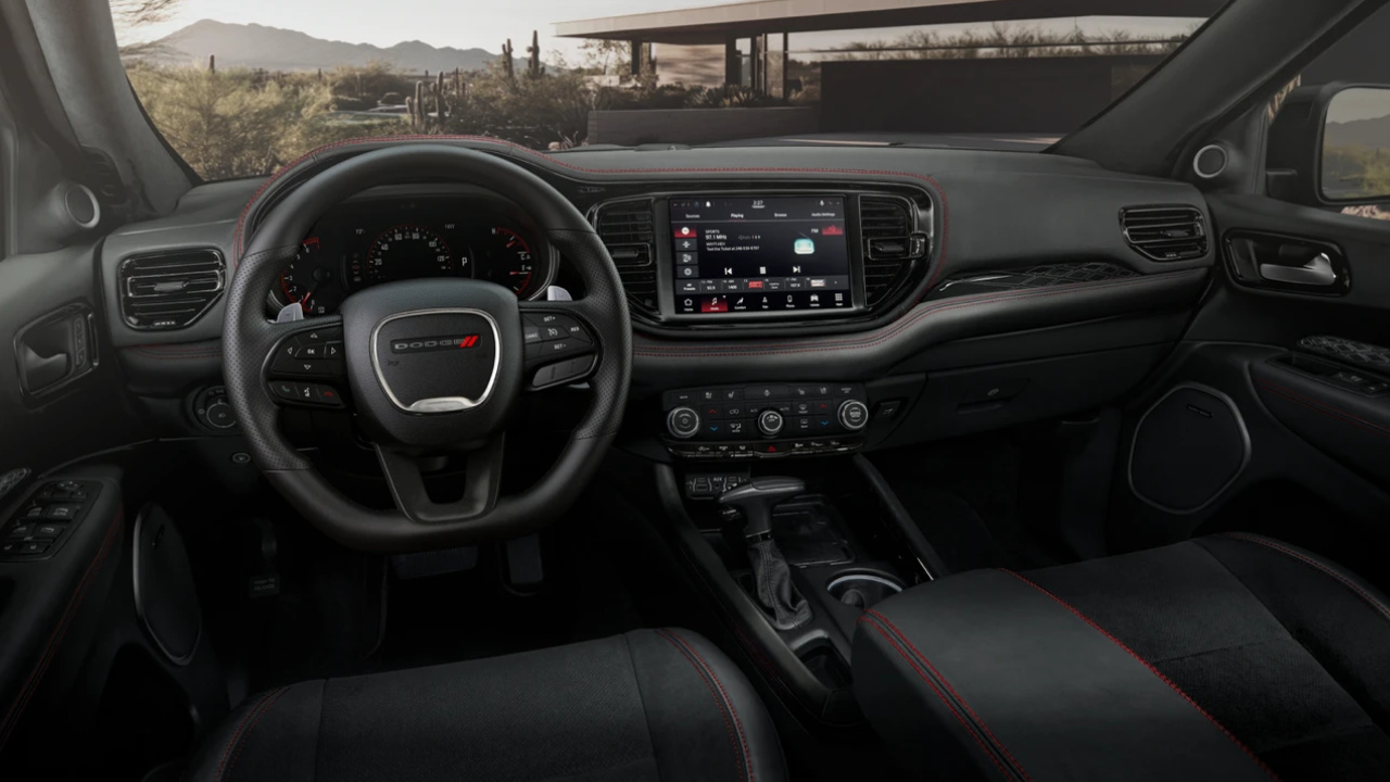 Vue intérieure du poste de conduite du Dodge Durango 2026 avec volant Dodge, écran central multimédia et finitions sport.