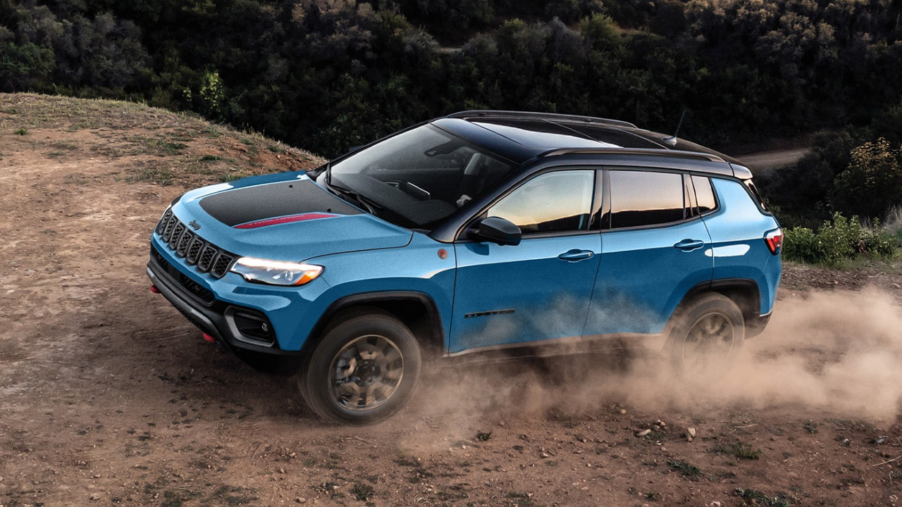 Vue aérienne du Jeep Compass 2026 bleu roulant sur un chemin de terre sinueux, démontrant ses capacités hors route et son système 4x4 en environnement naturel.