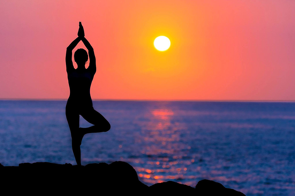 A woman in a graceful stretching pose on a beach at sunset, conveying a sense of peace and bodily flow.
