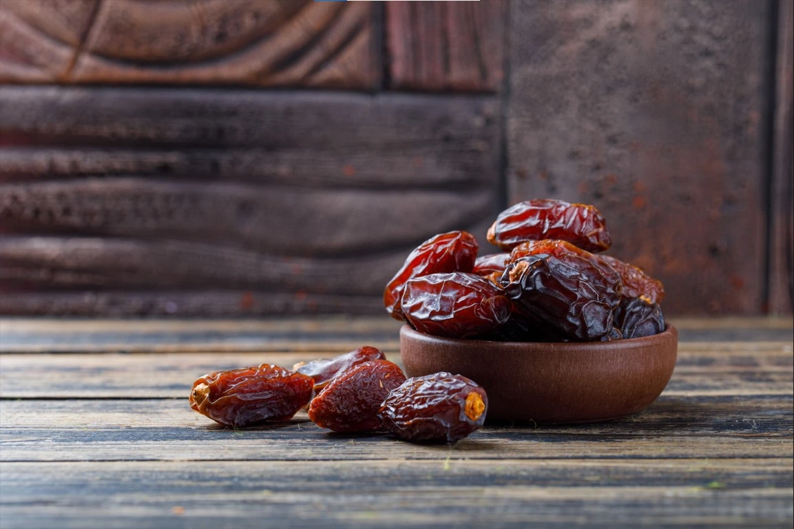 Sweet dates on a clay plate on a stone tile against a wooden background.