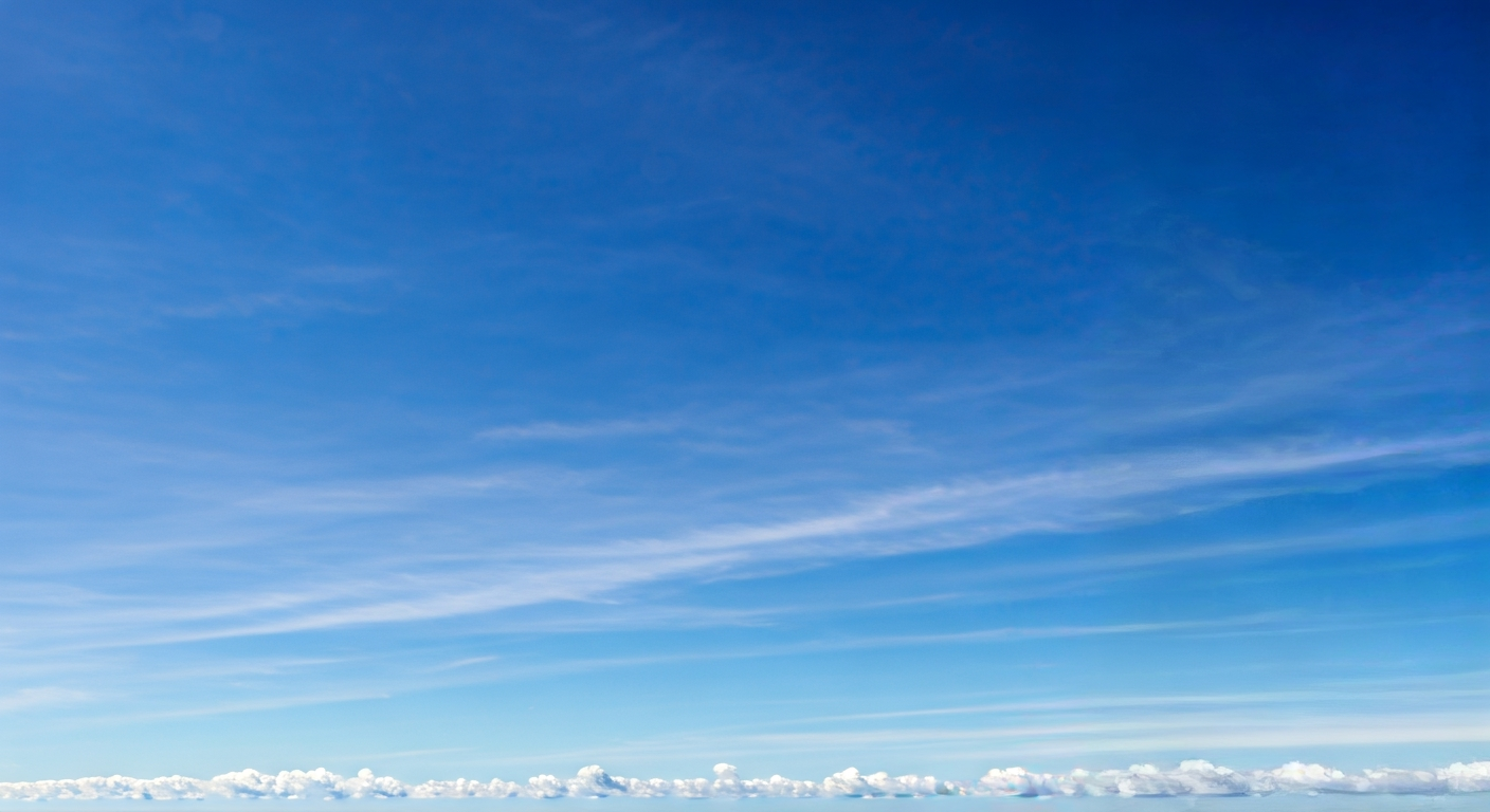 A vast, brilliant blue sky stretches overhead with a few delicate white clouds scattered near the horizon, illuminated by sunlight.