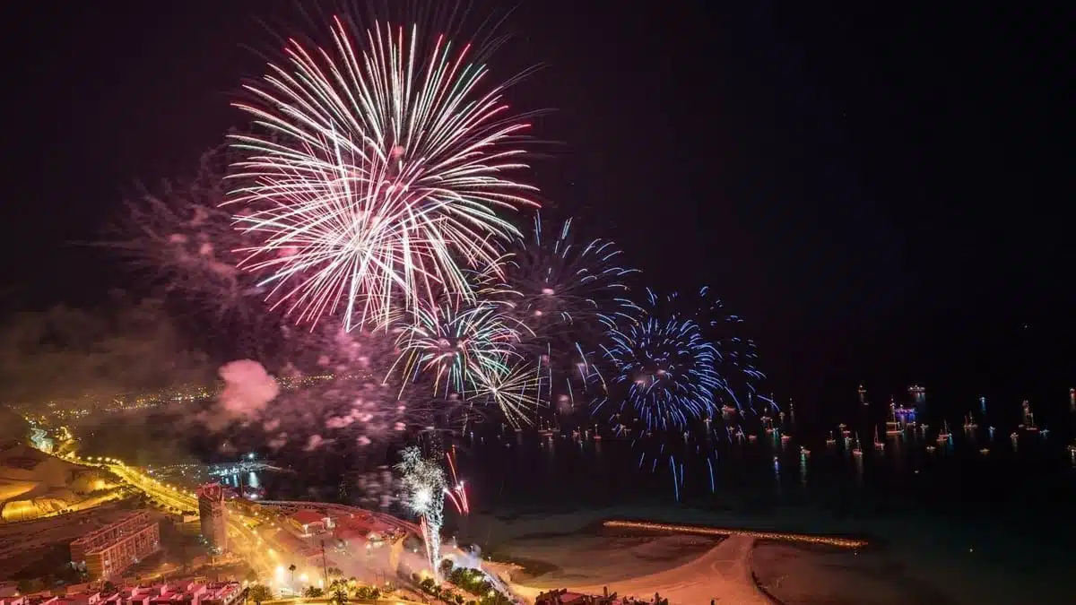Fuegos artificiales explotando sobre el mar por la noche, vistos desde un velero en Alicante.