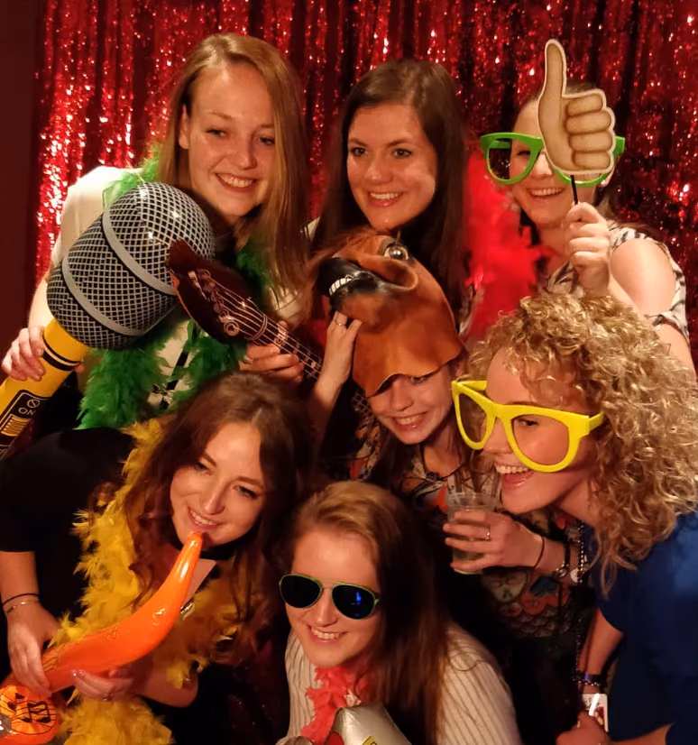 Groep feestgasten met props en een rode glitterachtergrond in de photobooth