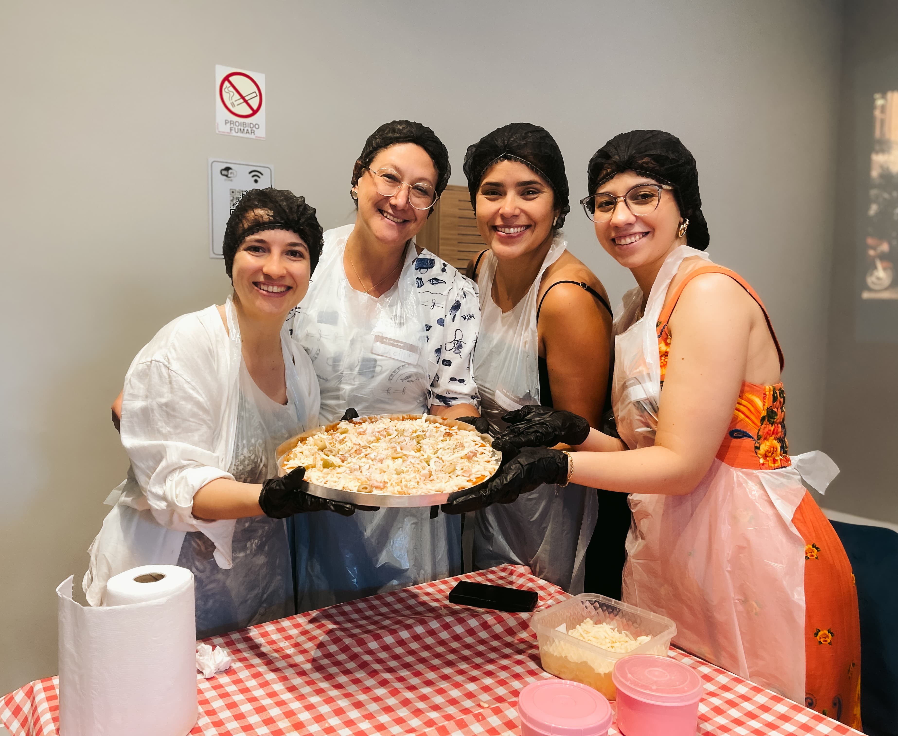 Colaboradores sorridentes trabalhando juntos na preparação da massa de pizza durante dinâmica de integração de equipe.