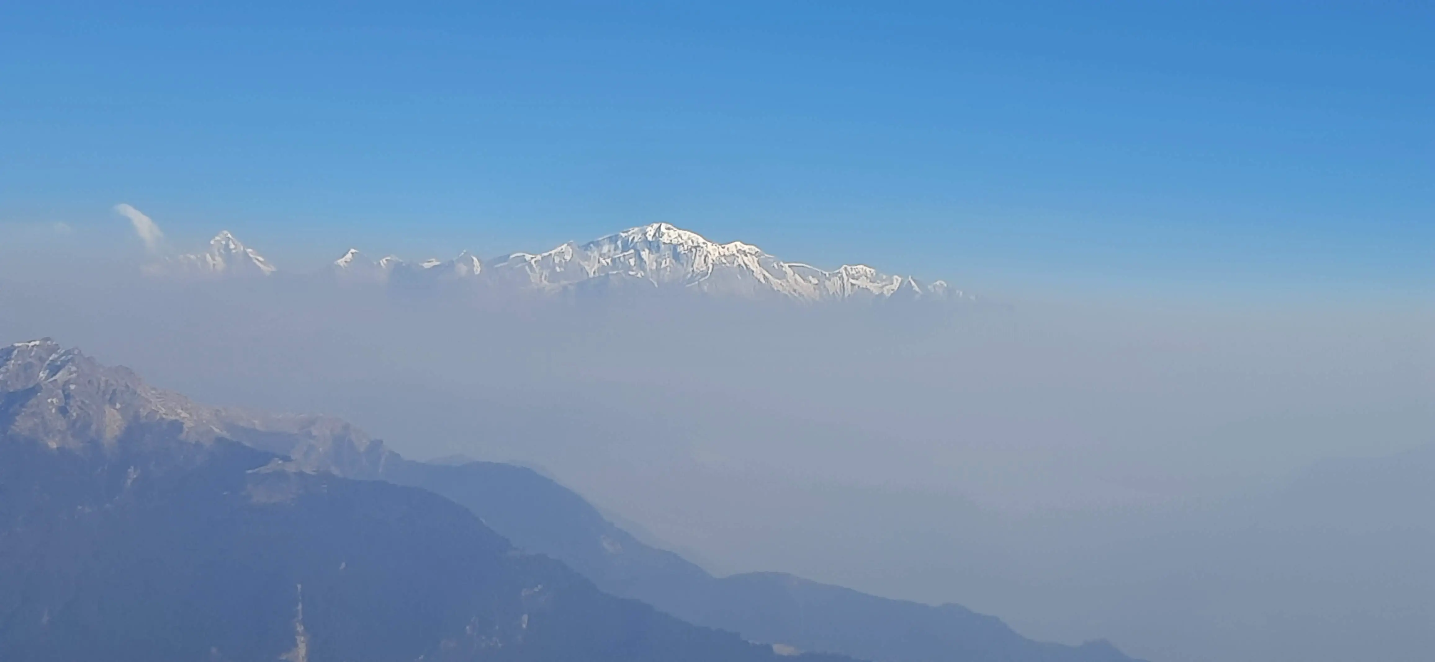 Snow-lit peaks hover beyond layers of haze present yet unreachable. This image marks the beginning of the journey, where the land is witnessed from afar and humility arrives before movement.
