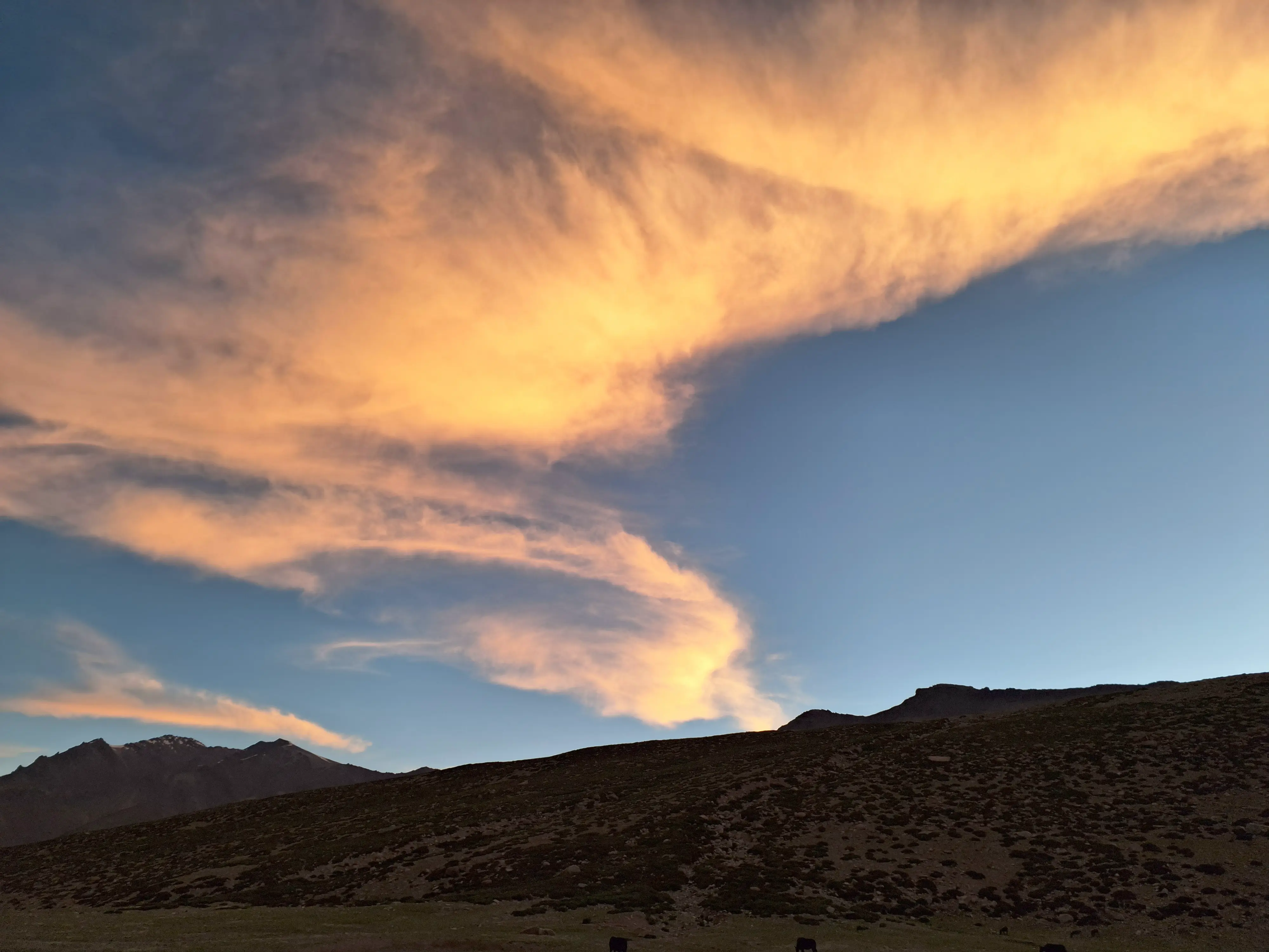 Clouds stretch like a moving border above dark ridgelines. The terrain feels paused as if waiting for permission to be entered.