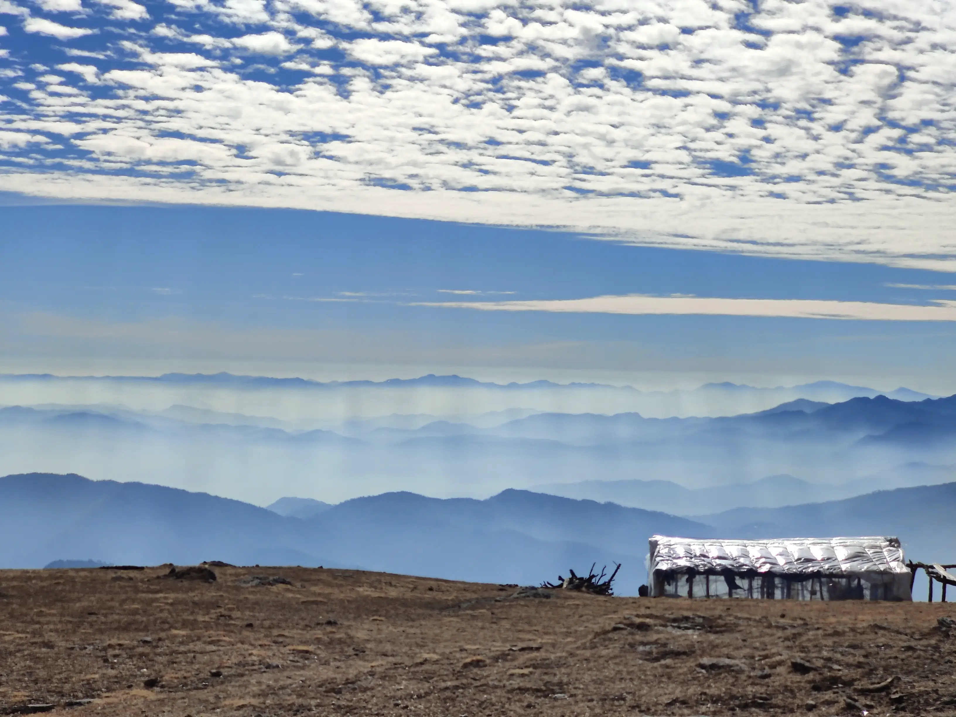Layered ranges dissolve into the horizon. A shelter clings to the land, reminding us that even permanence here is temporary.