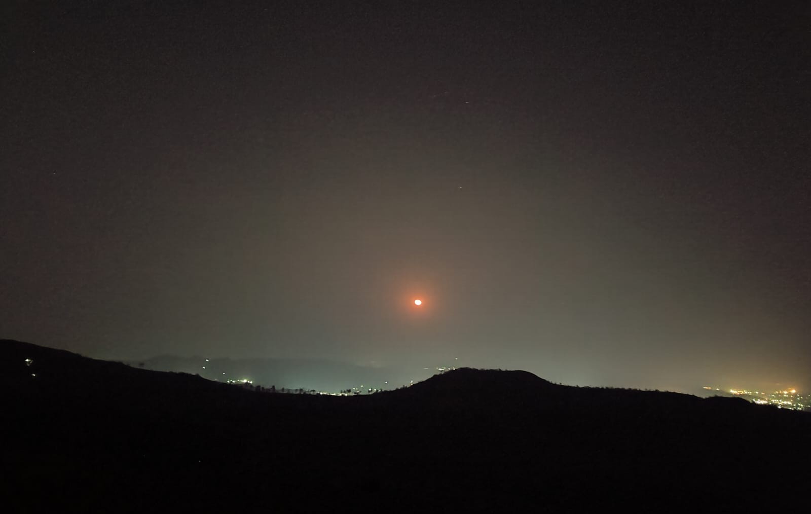 A group of trekkers resting on a hill with city lights in the distance.