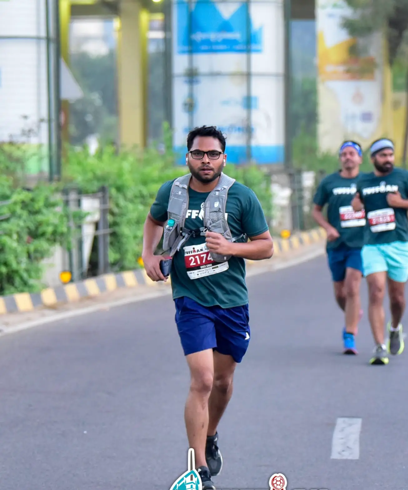 A climber standing at a high-altitude pass surrounded by prayer flags, with rugged Himalayan peaks stretching into the distance under a clear blue sky.