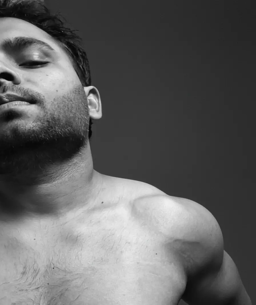 A climber standing at a high-altitude pass surrounded by prayer flags, with rugged Himalayan peaks stretching into the distance under a clear blue sky.