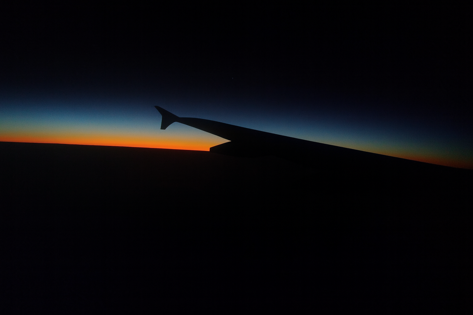 From the airplane window, the horizon divides darkness and light — a fleeting threshold between day and night.