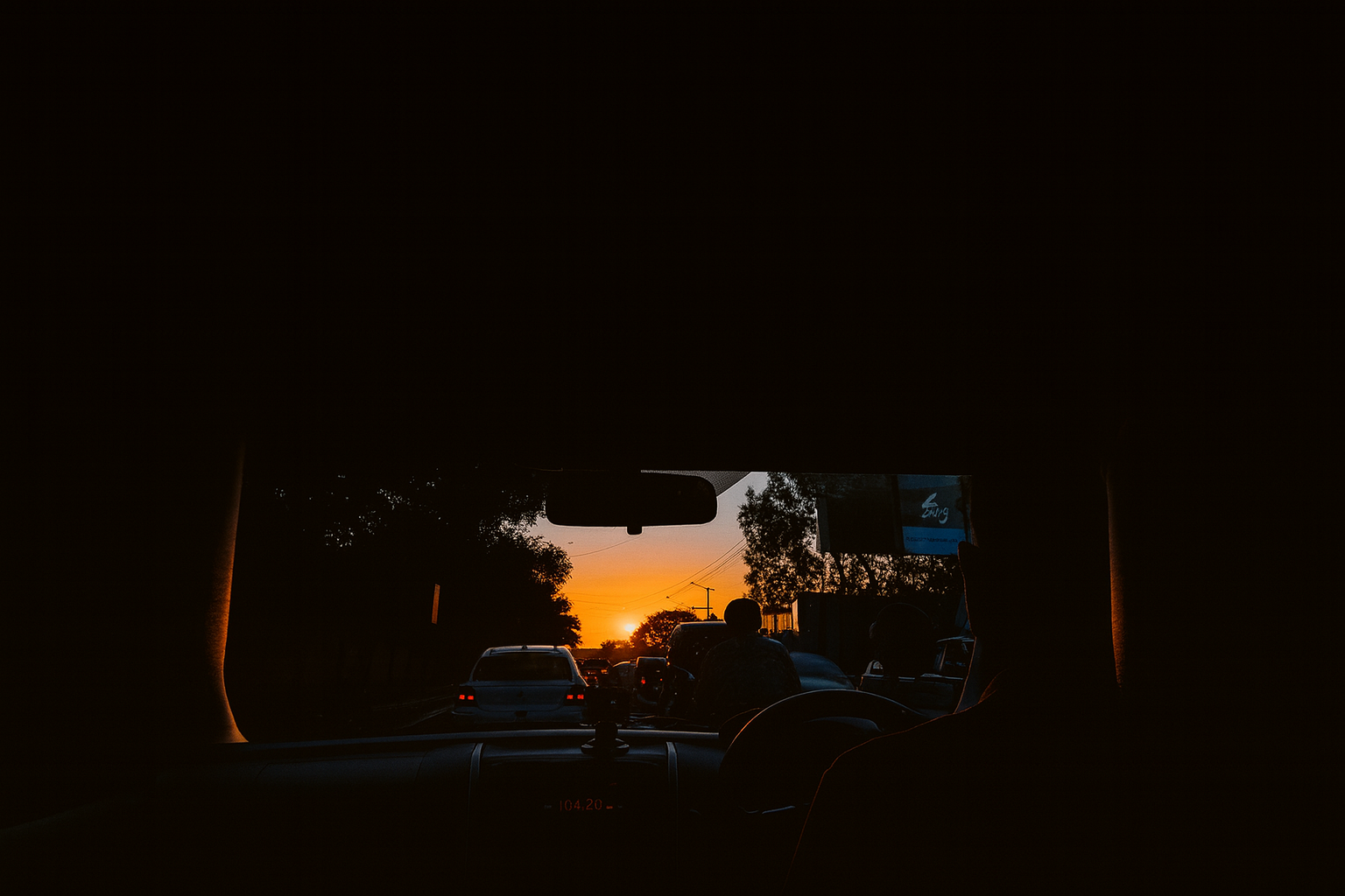 The sun sets beyond the windshield as traffic halts — an image of the human condition: moving endlessly, but paused inside.