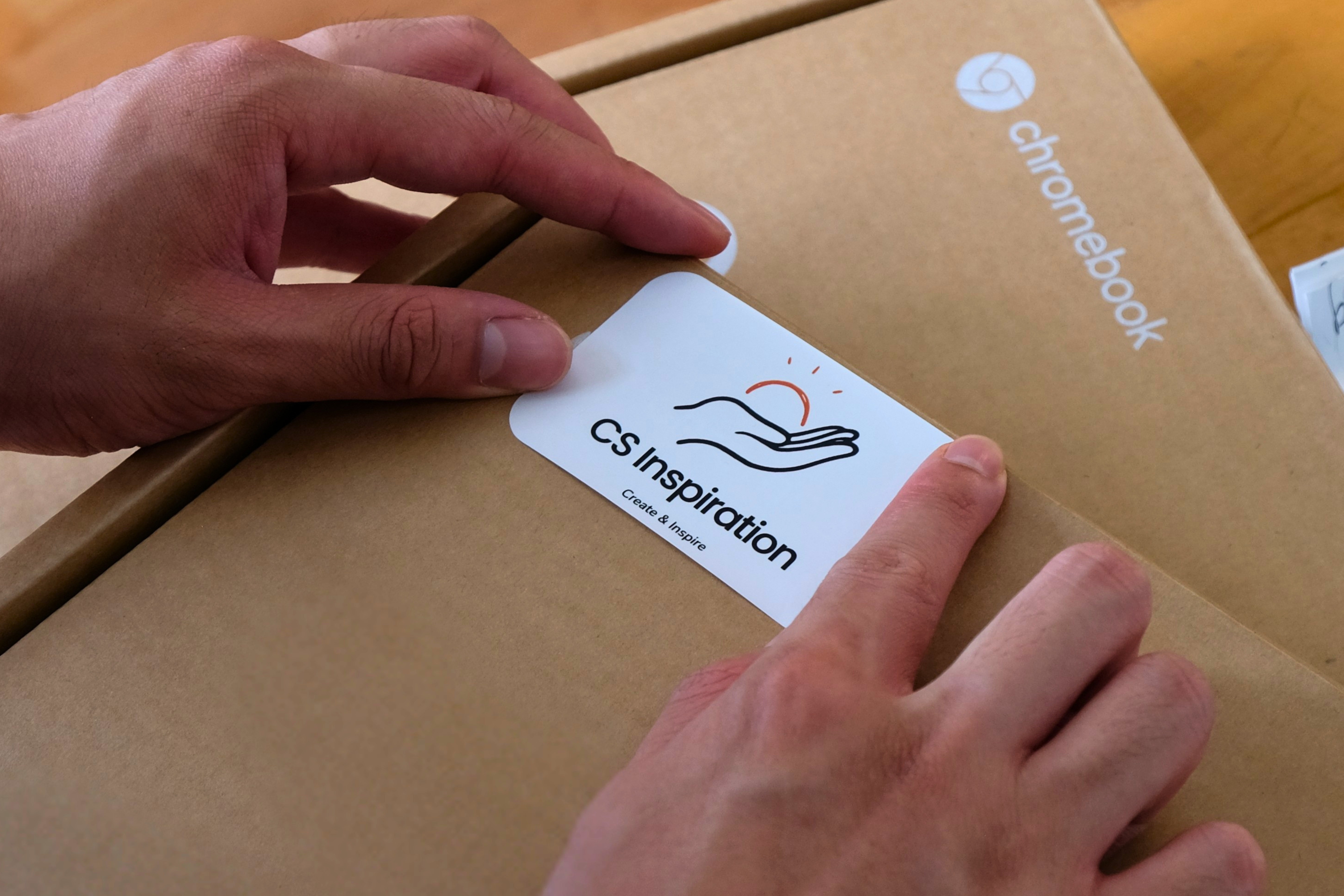 Hands placing a CS Inspiration card on a Chromebook box being prepared for the field.