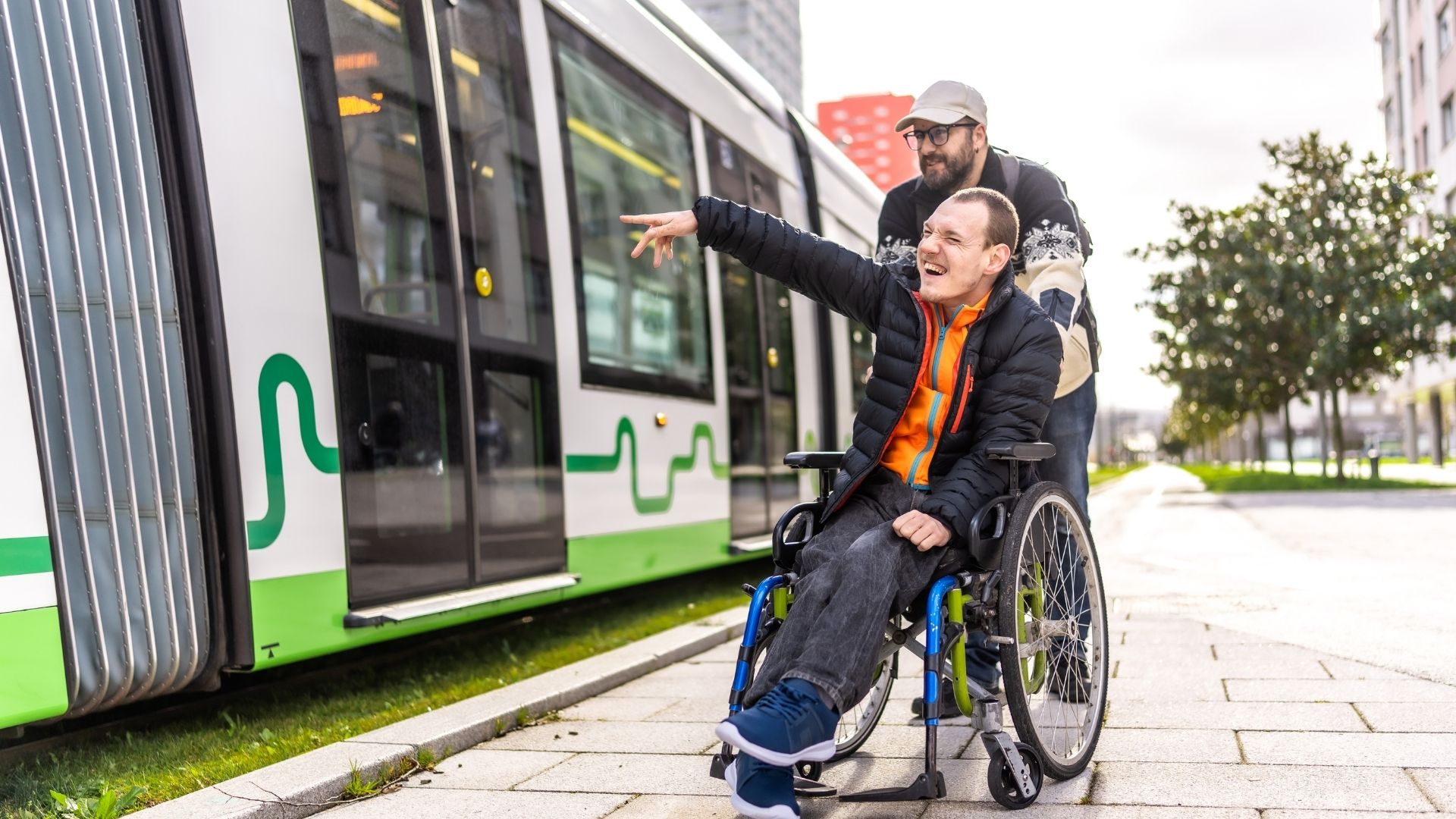 Disabled person pointing while sitting in wheelchair next to tram with friend.