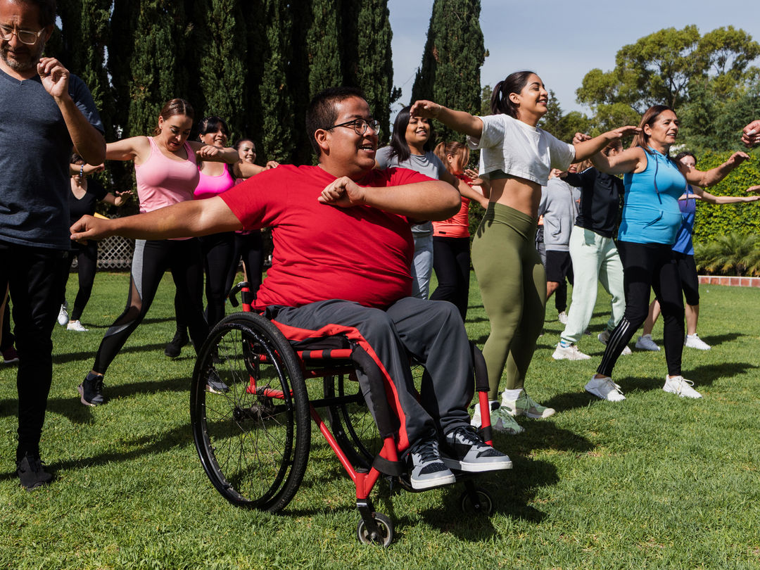 Sporty multi age people and disabled man in wheelchair in Zumba class outdoors