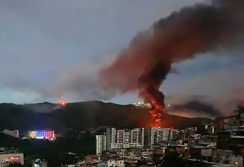 Um incêndio no Forte Tiuna, o maior complexo militar da Venezuela, é visto à distância após uma série de explosões em Caracas, em 3 de janeiro de 2026