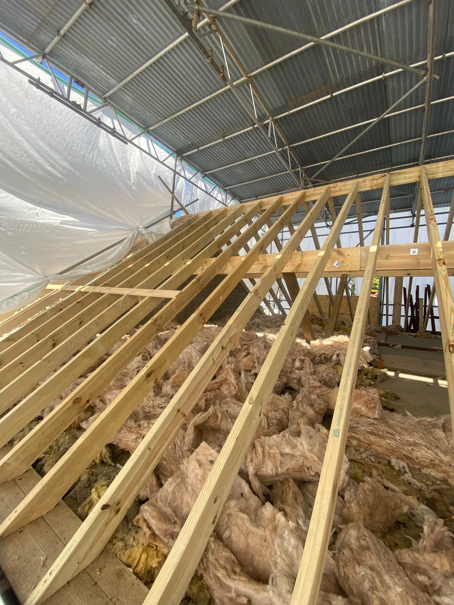 New rafters and a bolted purlin under a temporary scaffold roof, with loose mineral wool insulation below