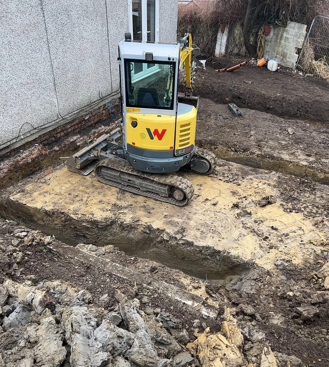 Mini excavator digging foundation trenches in wet winter ground on a Brislington plot