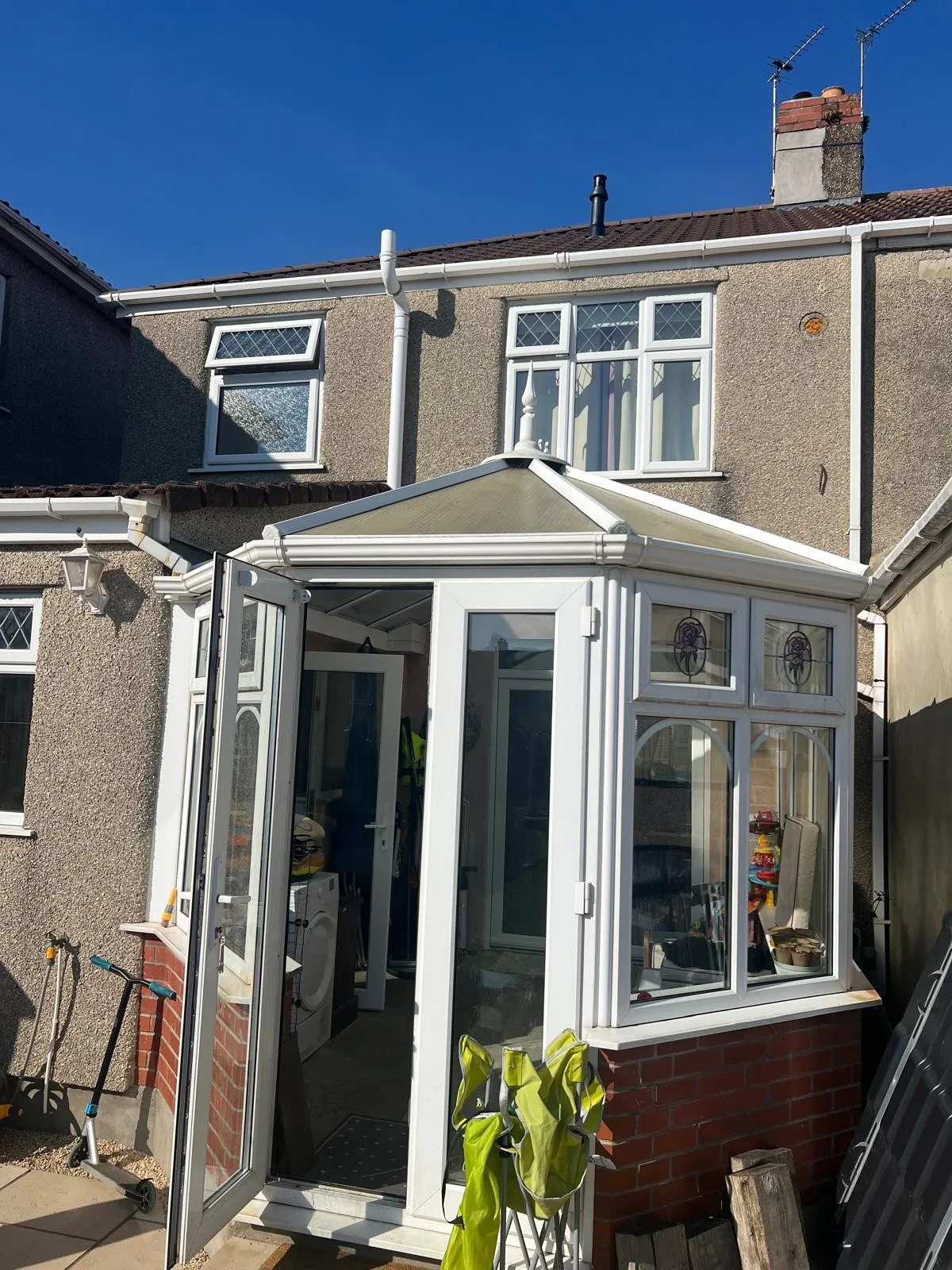 Old white uPVC conservatory on a low brick wall at the back of a pebble-dashed house in Kingswood