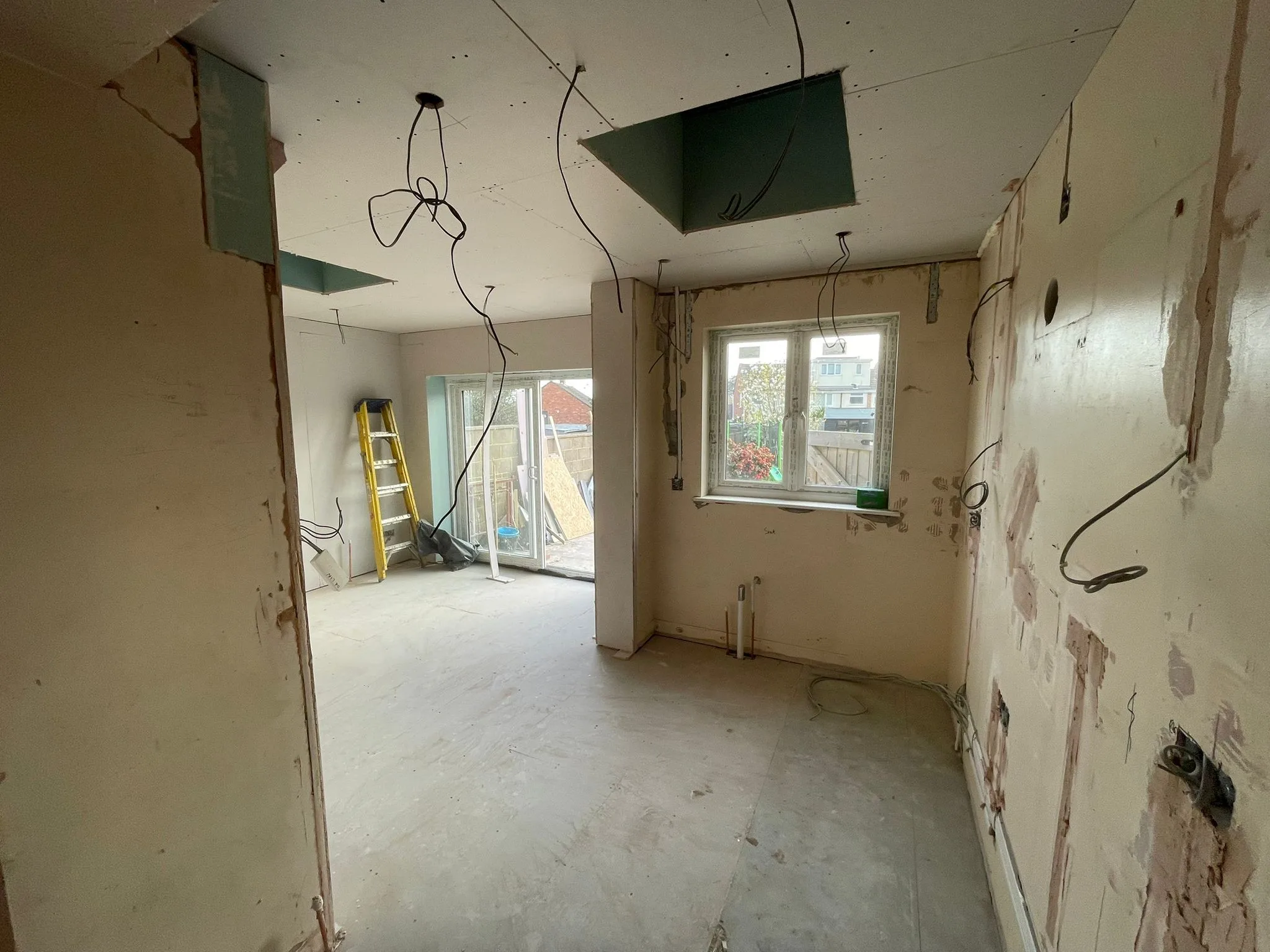 Extension interior at first fix with plasterboard ceiling, two rooflight openings, cables hanging and sliding doors fitted