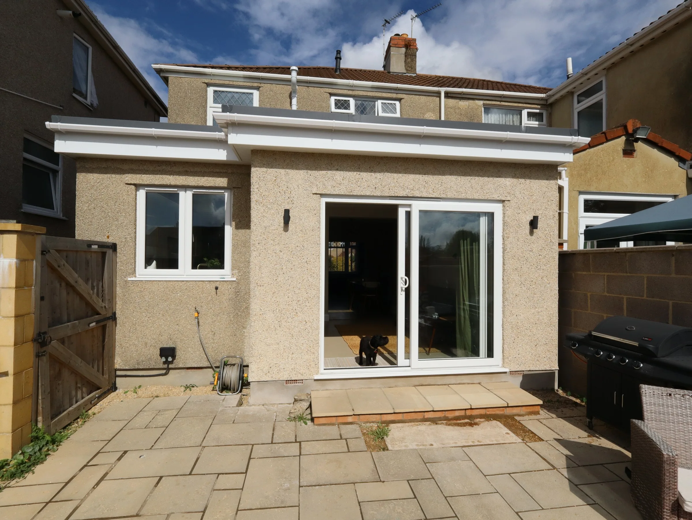 Finished rendered flat-roof rear extension with white sliding doors and a window opening onto a paved patio