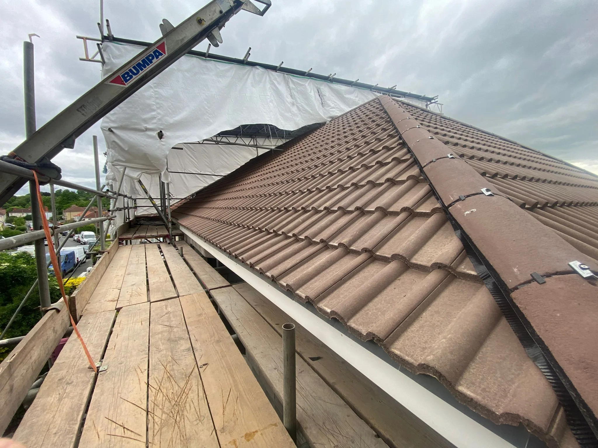 Brown double roman roof tiles and a dry-fixed hip on a new roof, seen from the scaffold with Brislington houses below