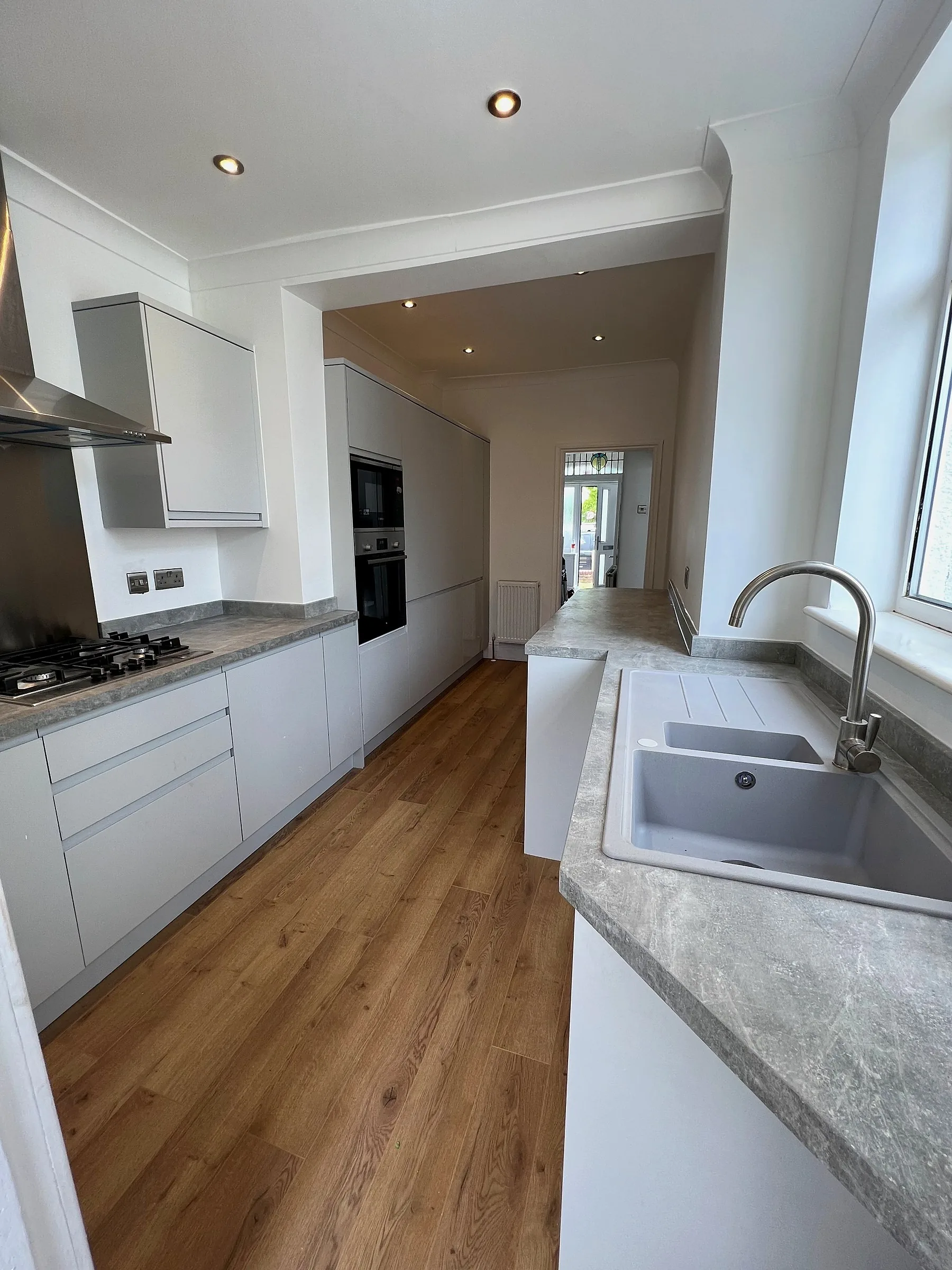Finished galley kitchen with pale grey units, grey worktops and a wood floor