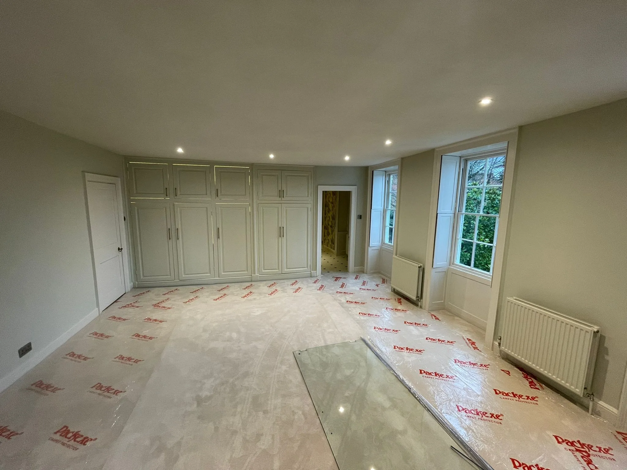 Georgian bedroom with fitted panelled wardrobes, sash windows and shutters, floor covered in protection film