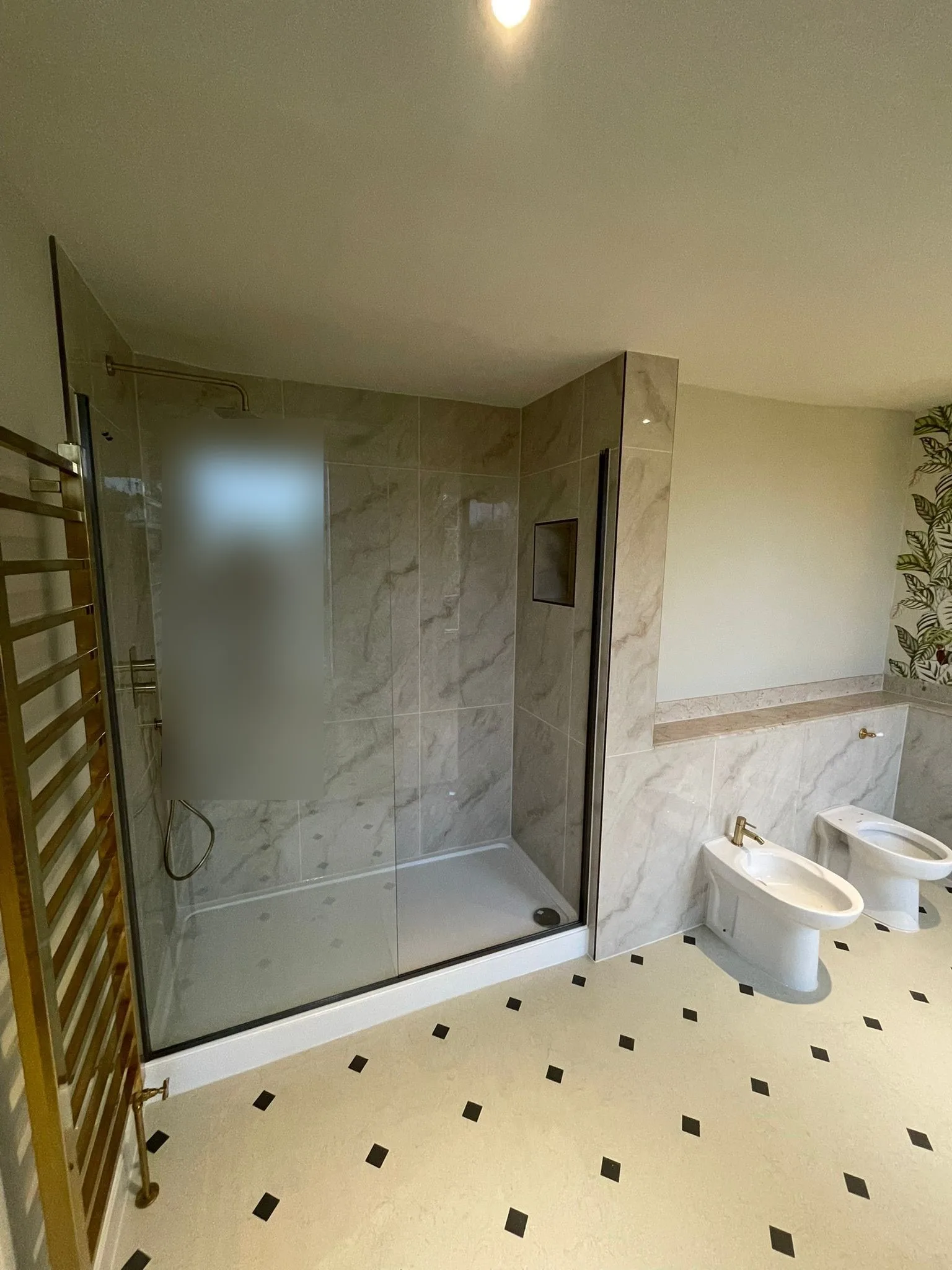 Walk-in shower with large marble-effect tiles, glass screen, brass fittings and a brass towel rail