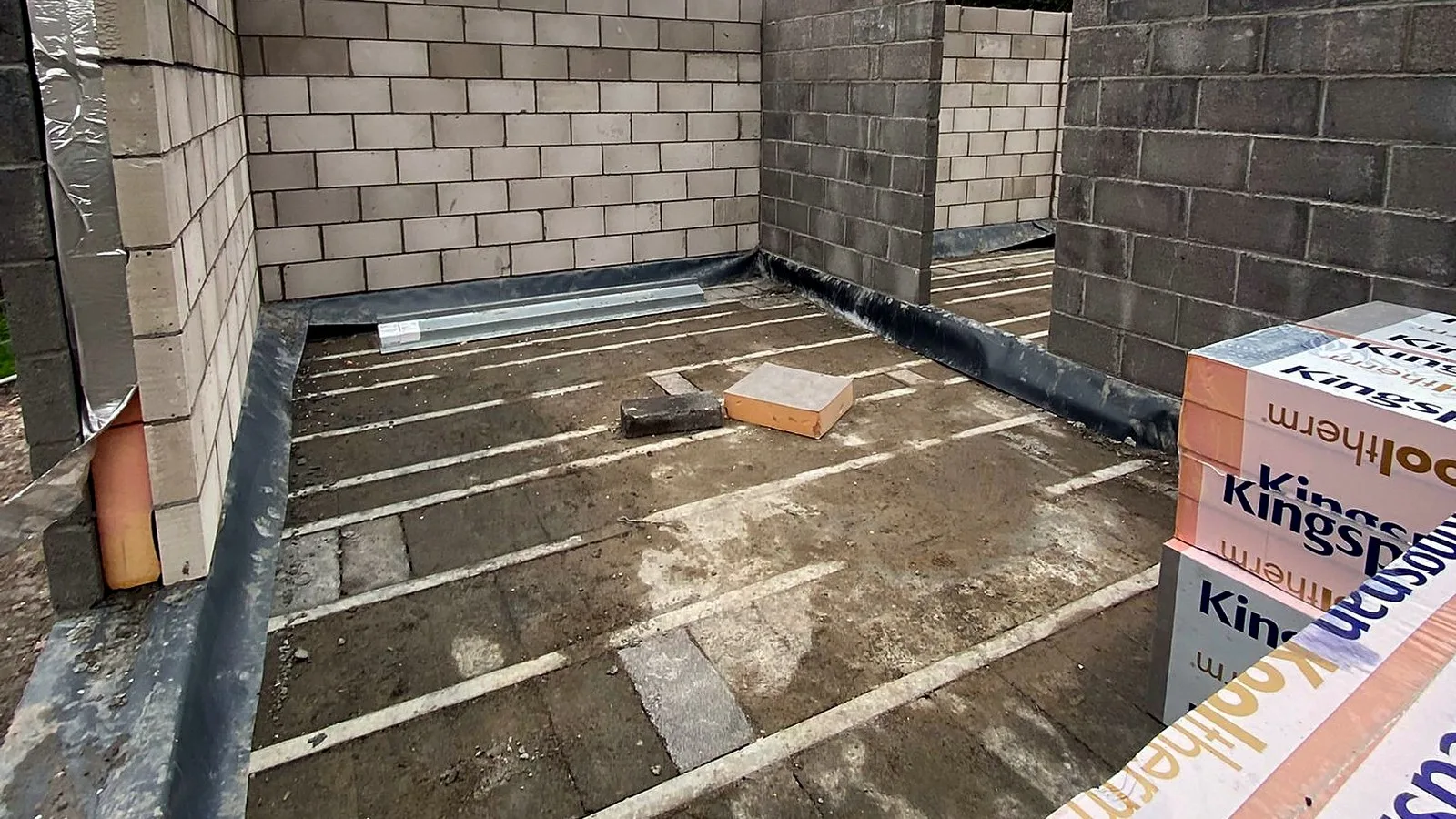 Groundworks for an extension in practice: a block and beam floor between new blockwork walls, insulation boards stacked