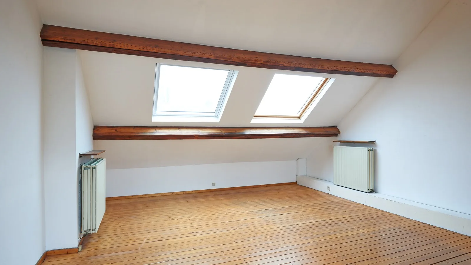 L shaped dormer loft conversion guide: a bright, empty loft room with two rooflights, timber beams and a wooden floor