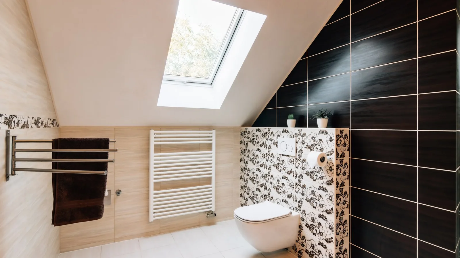 Loft conversion bathroom with a rooflight in the sloping ceiling, a wall-hung WC and dark wall tiles