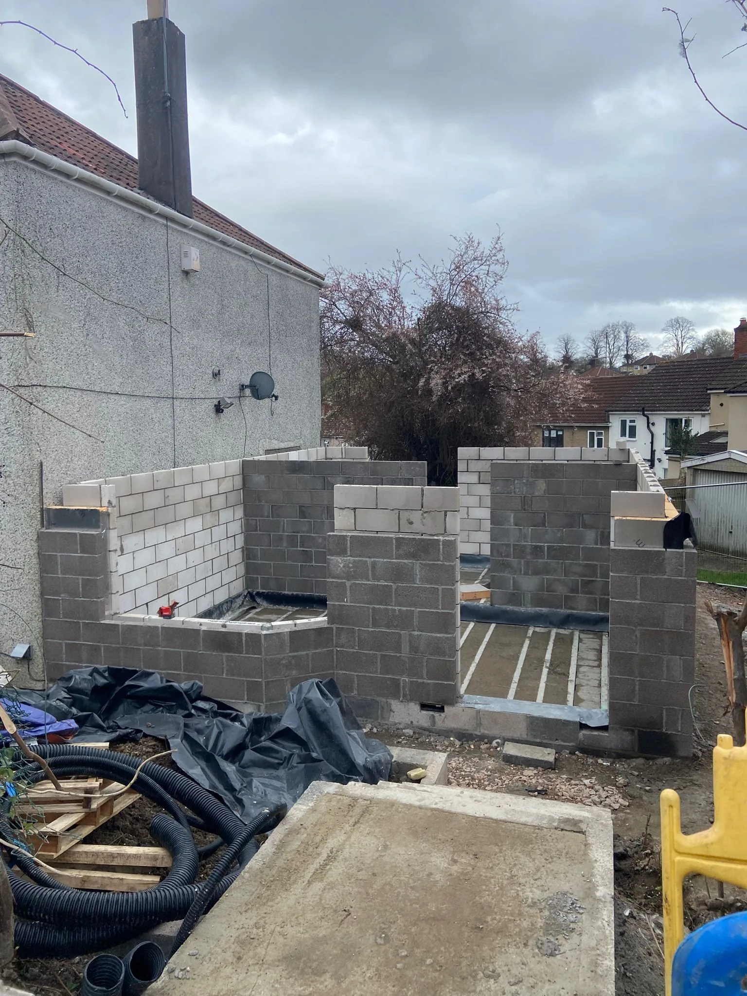 Blockwork walls rising beside the neighbouring rendered house, block-and-beam ground floor laid between them