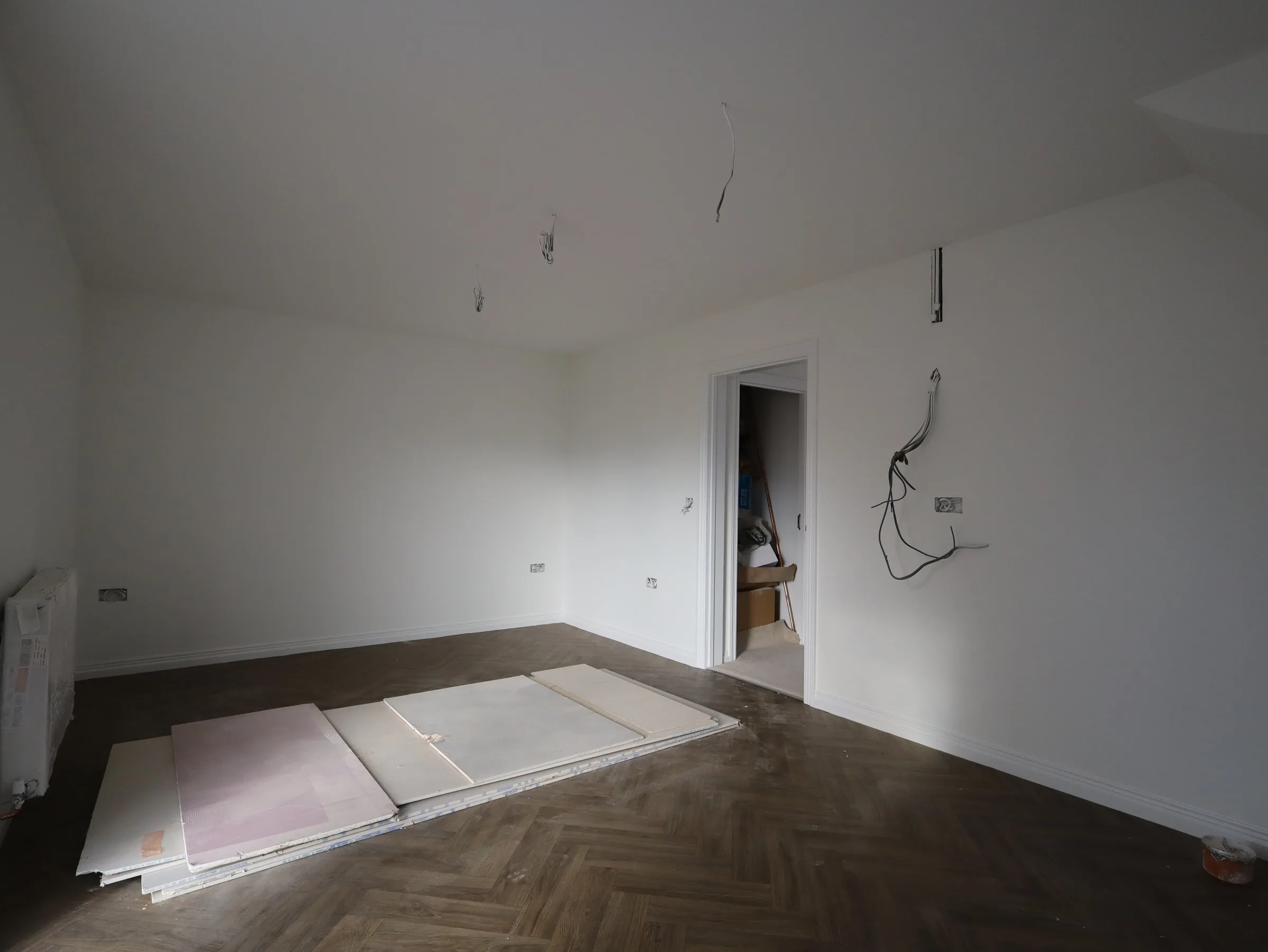 Ground-floor room with dark herringbone parquet laid, walls painted white and second fix still to come
