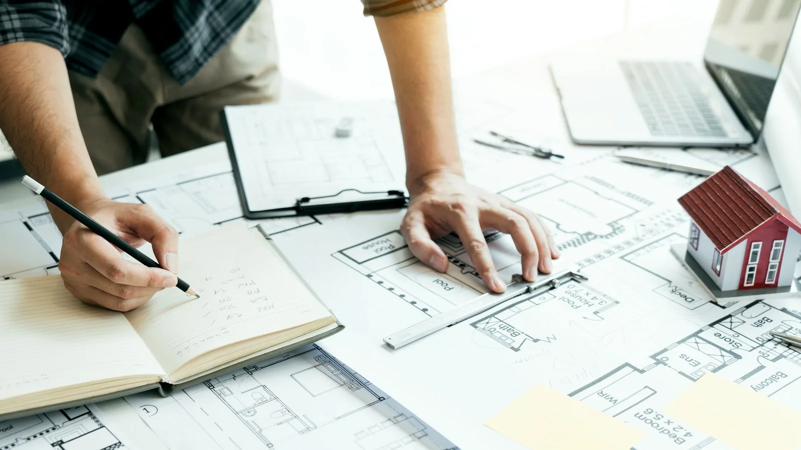 When to plan an extension: hands making notes over house floor plans, with a ruler and a small model house