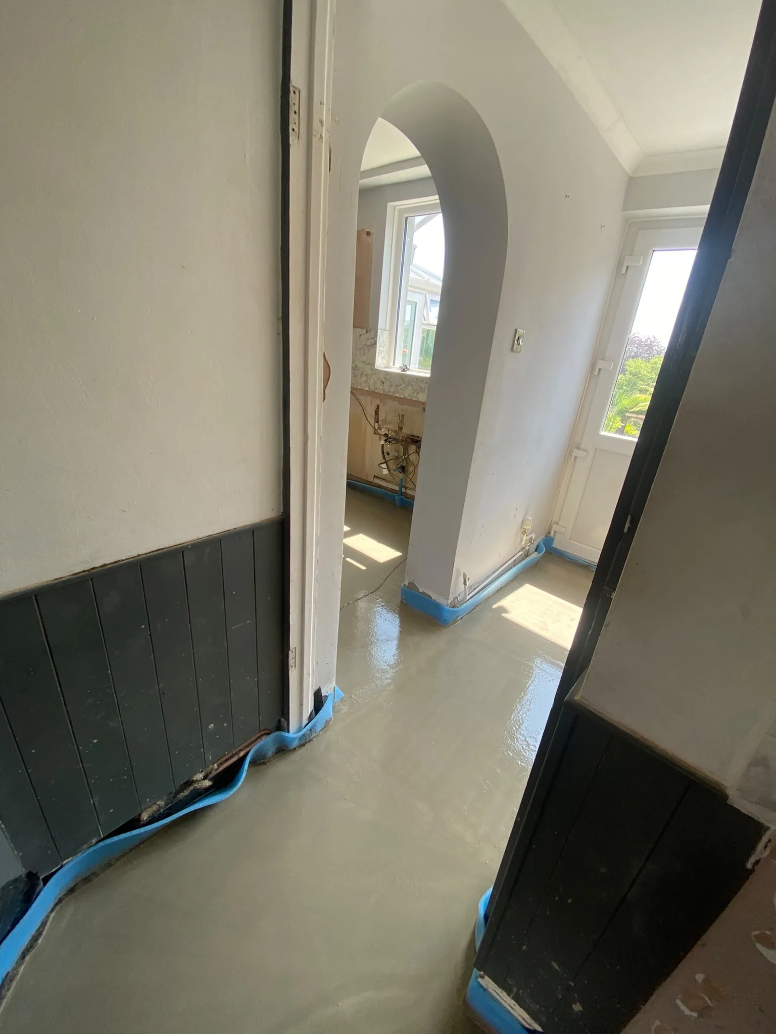 Freshly laid screed running through a hallway and under an arch into the kitchen