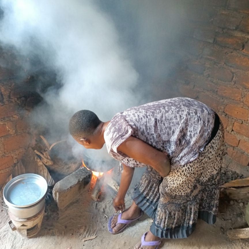 A woman cooking over a smoky, traditional fire.