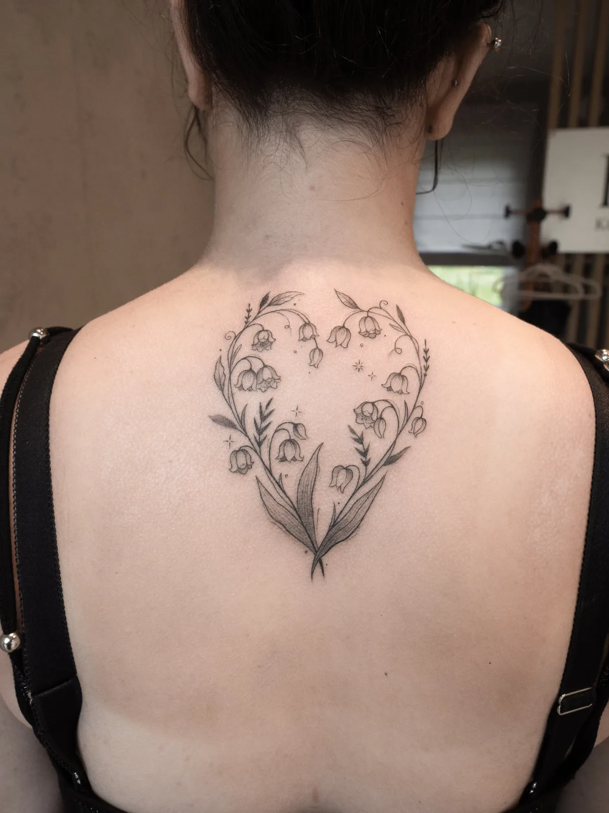Tatuaż z konwalii ułożonych w kształt serca na plecach, w stylu fineline.