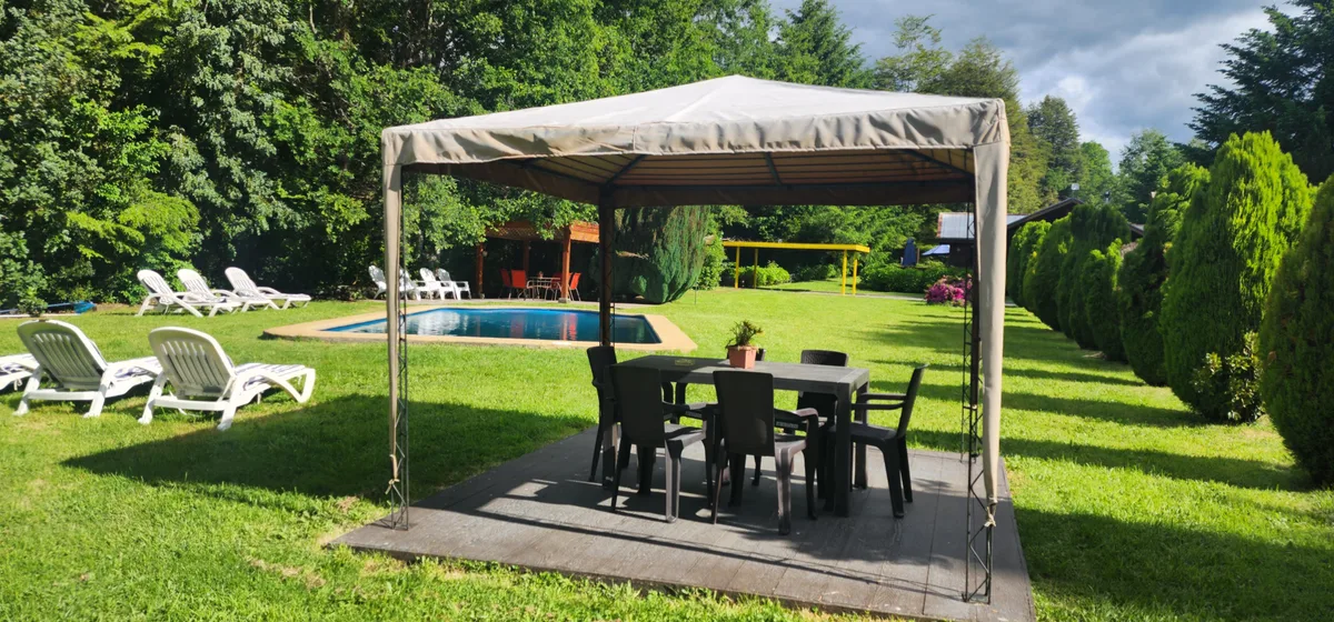 Área común exterior con piscina, tumbonas y zona de comedor cubierta en un entorno natural y verde.