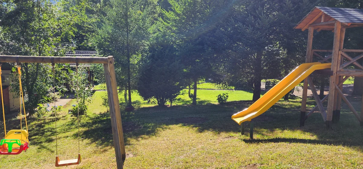 Zona de juegos infantil con columpio y tobogán de madera en área común de Prueba 1. Diversión para niños.