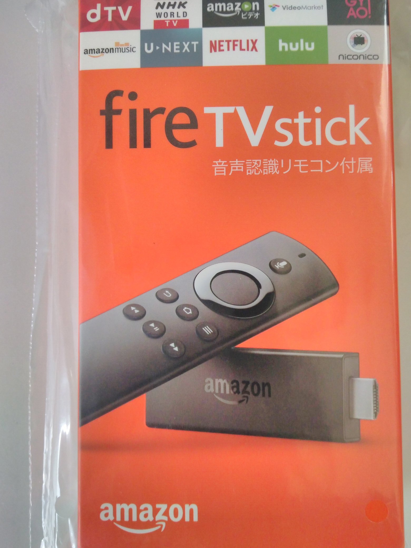 Fire TV Stickのオレンジ色の外箱。パッケージには立てられたFire TV Stickによりかかるようにそのリモコンが乗っている構図の写真です。