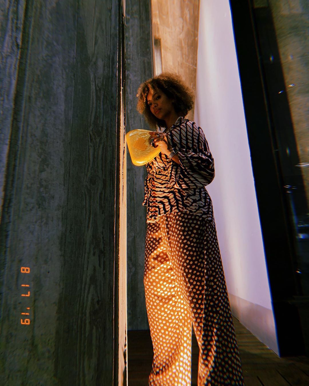 Alyssa Simone poses against a cement wall wearing a striped sweater and polkadot skirt.