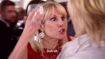 A blond woman gets in another woman's face with a wine glass in her hand as she yells, "Duh-uh"