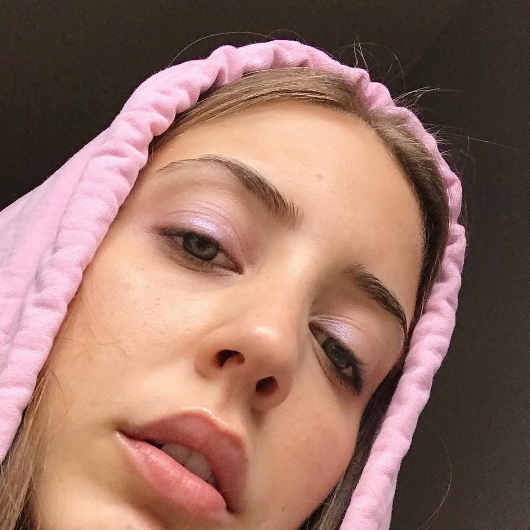 Savannah wears a pale pink eyeshadow on her lids that matches the hood of her pale pink hoodie around her head in a selfie.
