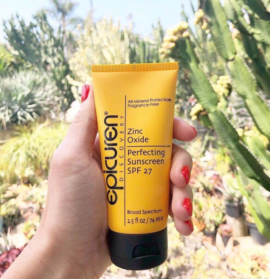 A hand holds Epicuren's Zinc Oxide Sunscreen in front of desert plants.